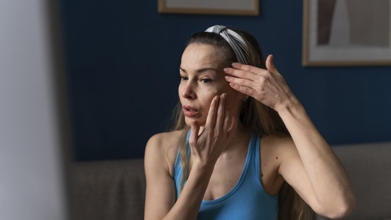 Взрослая женщина смотрит в зеркало, обвисание кожи